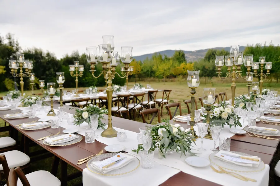A long outdoor reception table set with flowers, glassware and candelabras.