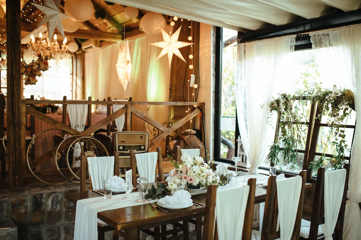 A rustic wedding reception with decorated tables beneath timber beams.